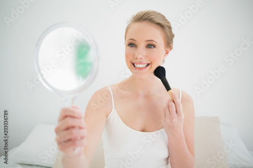 Natural smiling blonde holding mirror and using brush