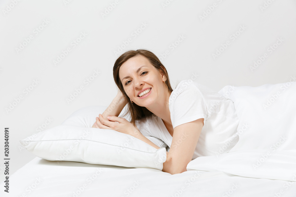Calm young brunette woman lying in bed with white sheet, pillow, blanket on white background. Smiling beauty female spending time in room. Rest, relax, good mood concept. Copy space for advertisement. Calm young brunette woman lying in bed with white sheet, pillow, blanket on white background. Smiling beauty female spending time in room. Rest, relax, good mood concept. Copy space for advertisement.