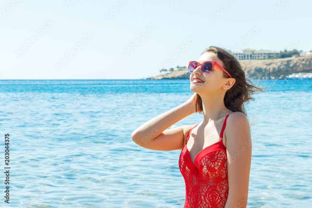 Beautiful happy brunette girl posing on the beach in a red bathing suit