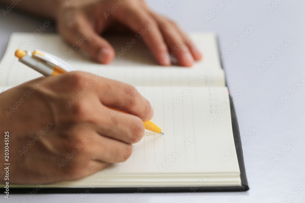 Hand of businessman hold a yellow pen writing to the note on paper book. Hand of businessman hold a yellow pen writing to the note on paper book.