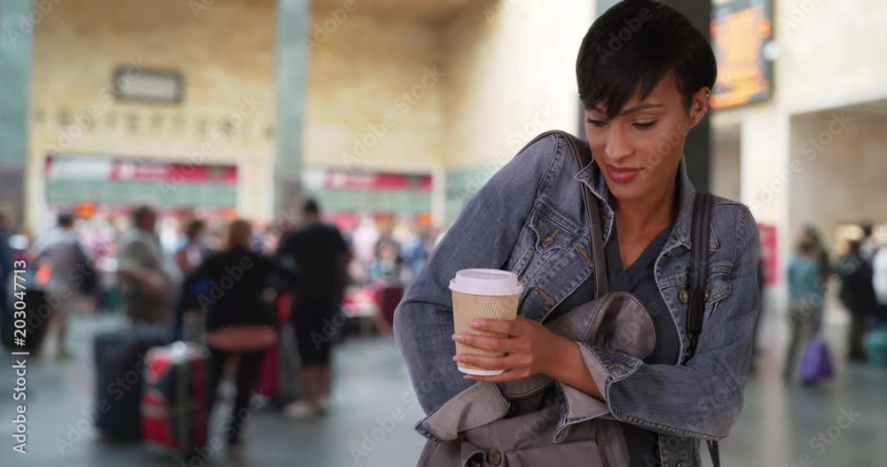 Gorgeous African woman takes her smartphone out of her purse to see a recent text message, Young African-American female at train station lobby with coffee checks her phone, 4k