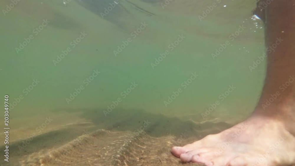 Underwater shot of feet walking on sandy ocean beach. The camera moves under the water. Underwater shot of feet walking on sandy ocean beach. The camera moves under the water.