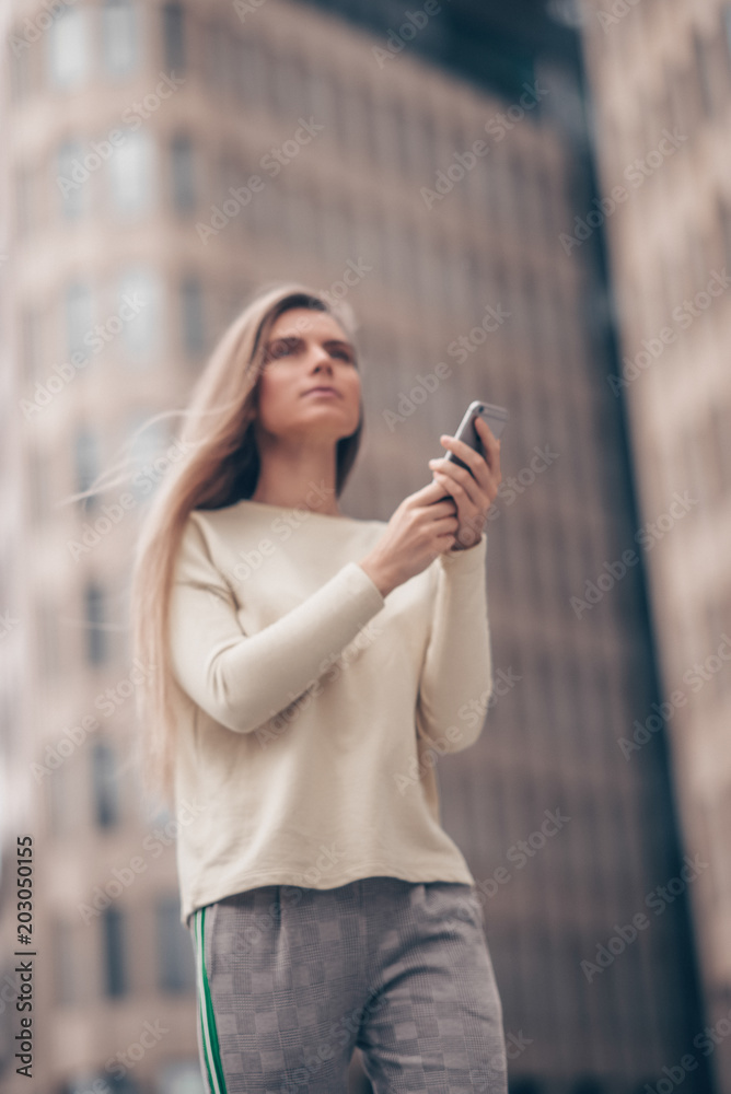Beautiful woman is out of focus and using a mobile phone near modern office building