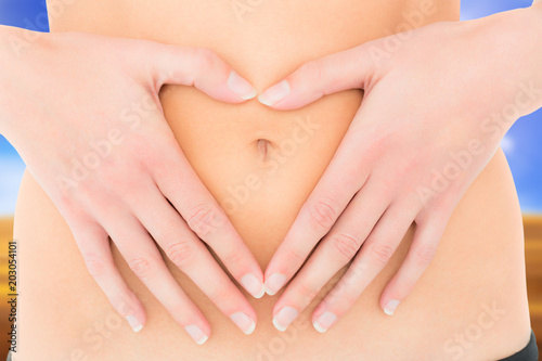 Mid section of a fit woman with hands over belly against sunny brown landscape