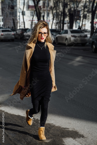 Fashion young girl in glasses. Blonde, red lips, beige coat walking along the city street. © photominus21