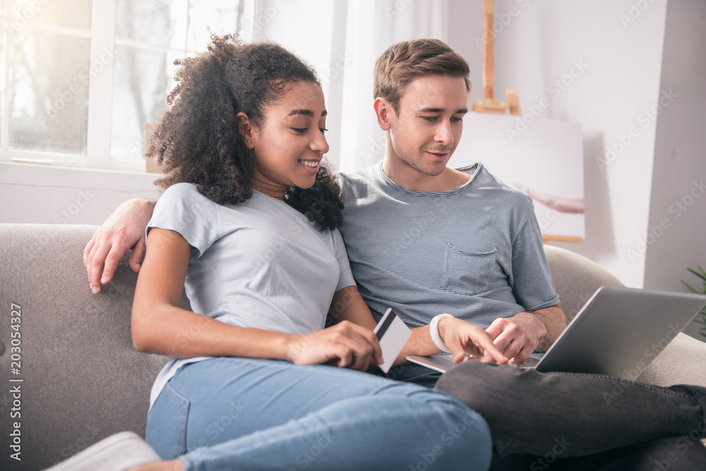 Joint activity. Joyful young couple sitting in front of the laptop while doing online shopping together Joint activity. Joyful young couple sitting in front of the laptop while doing online shopping together