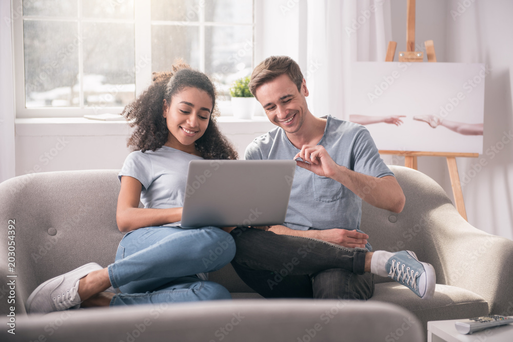 Family life. Happy pleasant couple sitting on the sofa while browsing the Internet together
