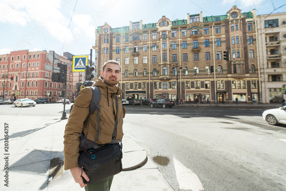 Young hipster man traveling backpacker outdoor in Saint-Petersburg street. He is on crossroads Travel, hiking concept