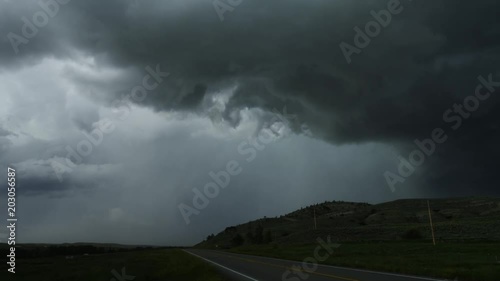 Dark clouds swirl above a highway along prairie hills, time lapse photo