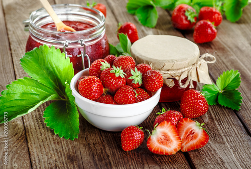 Homemade strawberry jam or marmalade in the glass jar and the basket of ripe strawberries on the wooden table