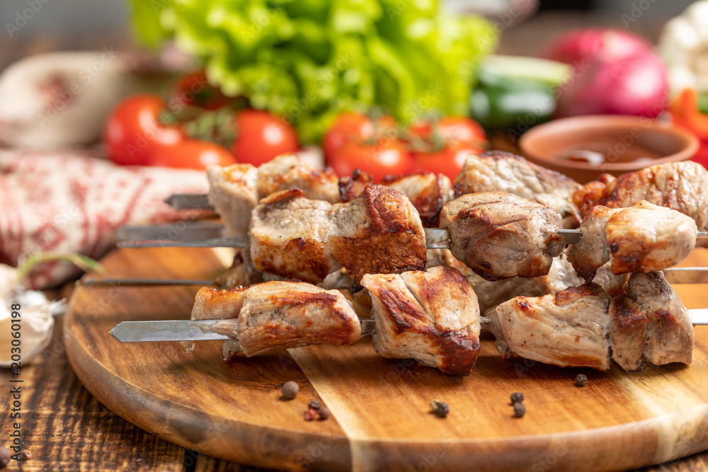 Juicy kebabs from pork on skewers laid out on a decorative board with fresh vegetables.