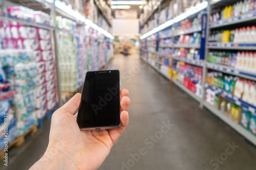 Hand with mobile phone on a background of a blurry shopping center