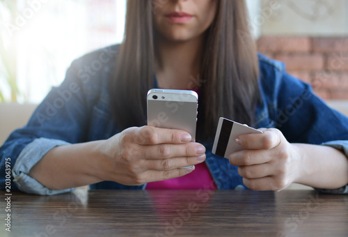 A brunette girl in a denim jacket is eating lunch in a cafe and using her phone. Communication through messenger. Casual loose clothing.