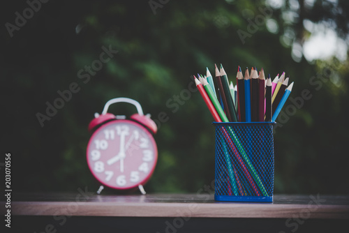 Alarm clock and colored crayons on the wooden table  with bokeh