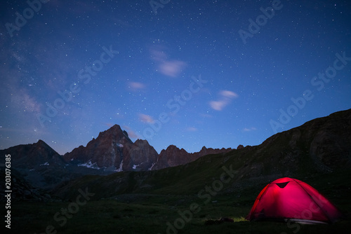 Camping under starry sky and milky way at high altitude on the Alps. Illuminated tent in the foreground and majestic mountain peak in the background. Adventure and exploration in summertime. © fabio lamanna