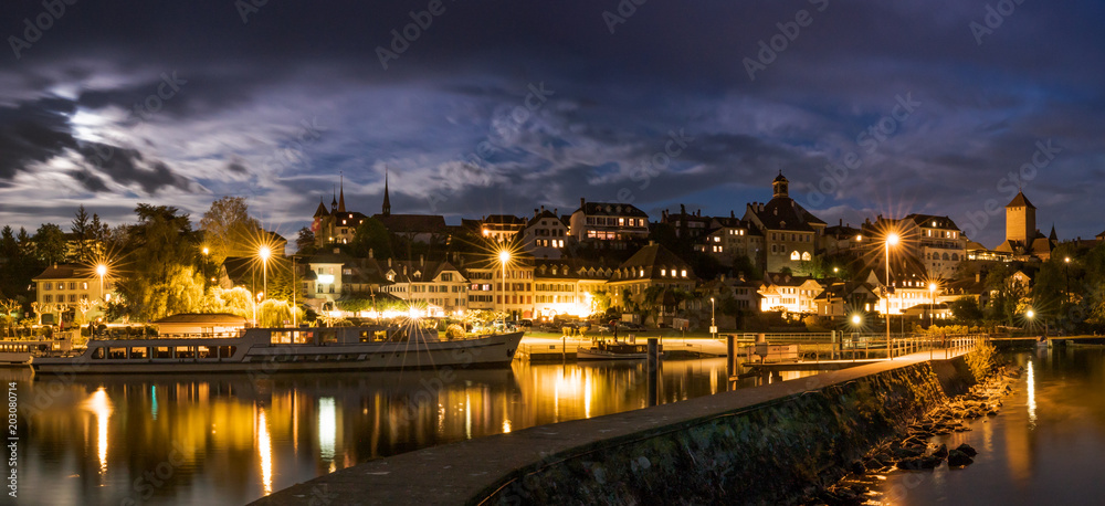 skyline at night  of Murten in Switzerland with the harbor and pier and boat in the foreground
