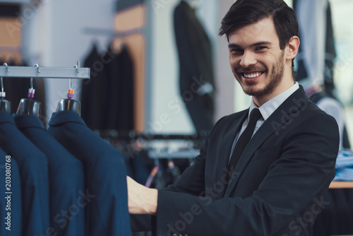 Fotografija Successful young businessman chooses jacket in store of mens presentable clothes