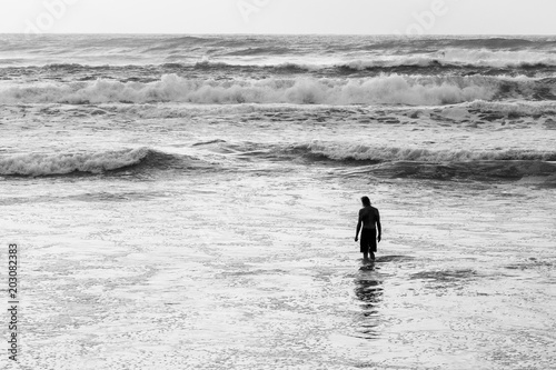 Silhouette of a man standing knee deep in ocean waves in black and white
