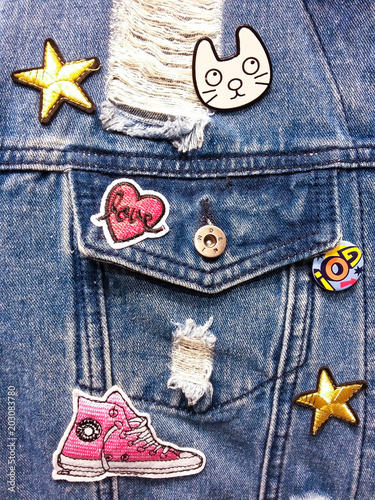 Vintage denim texture background: jacket close-up with pocket and colorful decor. Patches, embroidery, badge.