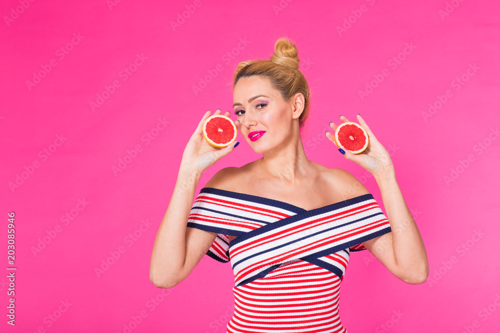 Young woman on a pink background holds a cut orange in her hands and laughs. Colour obsession concept. Young woman on a pink background holds a cut orange in her hands and laughs. Colour obsession concept.