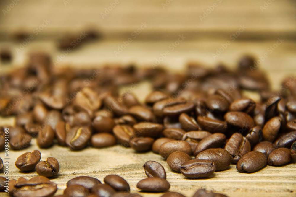 Coffee beans spilled onto a wood table with the focus on the beans near the viewer. Coffee beans spilled onto a wood table with the focus on the beans near the viewer.