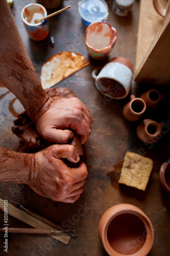 Hands of male potter molding a clay in pottery workshop, close-up, selective focus photo