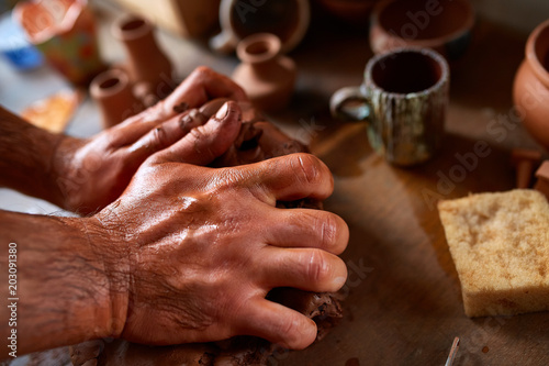 Hands of male potter molding a clay in pottery workshop, close-up, selective focus photo