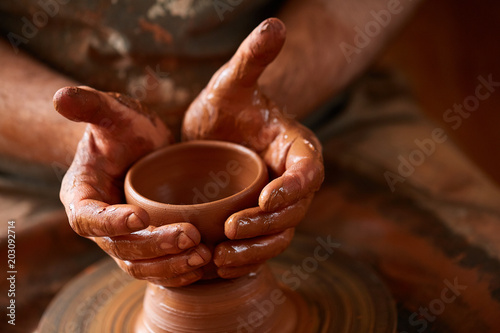Close-up hands of a male potter in apron molds bowl from clay, selective focus photo