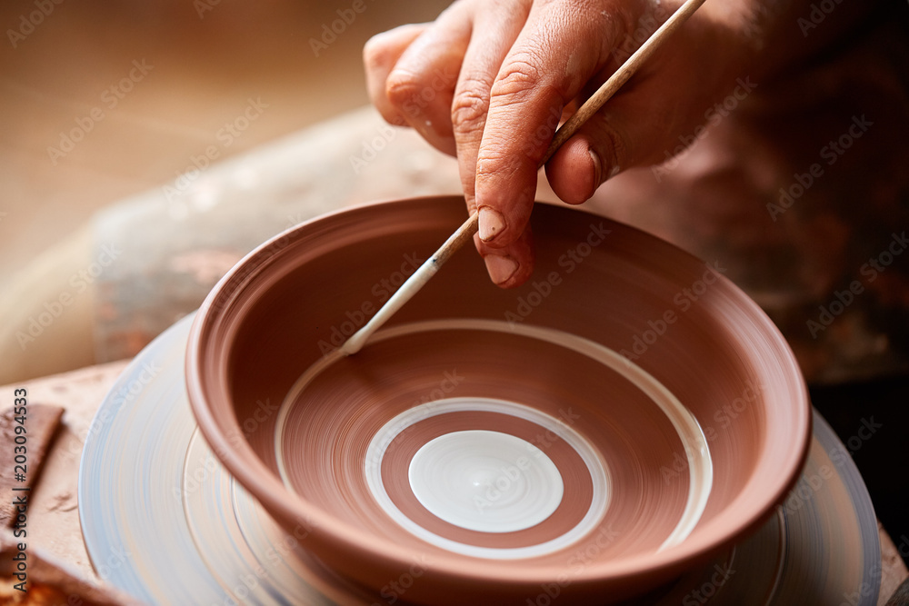 A potter paints a clay plate in a white in the workshop, top view, close-up, selective focus.