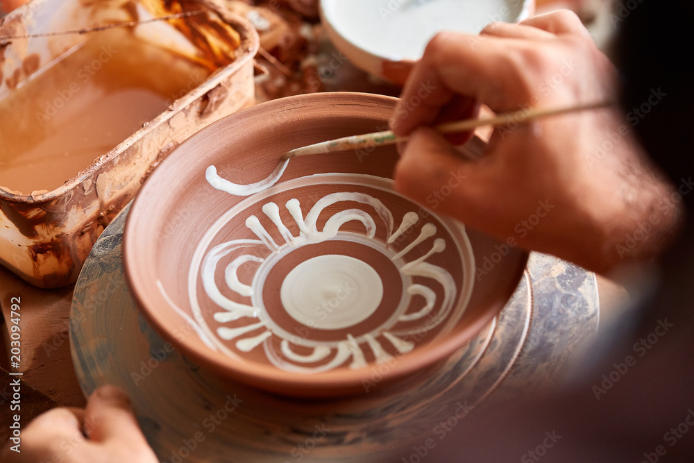 Fototapeta premium A potter paints a clay plate in a white in the workshop, top view, close-up, selective focus.