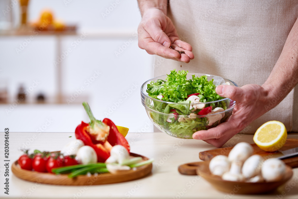Man cooking at kitchen making healthy vegetable salad, close-up, selective focus.
