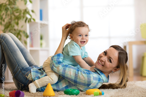 Happy mother and baby son lying on the floor and playing indoor