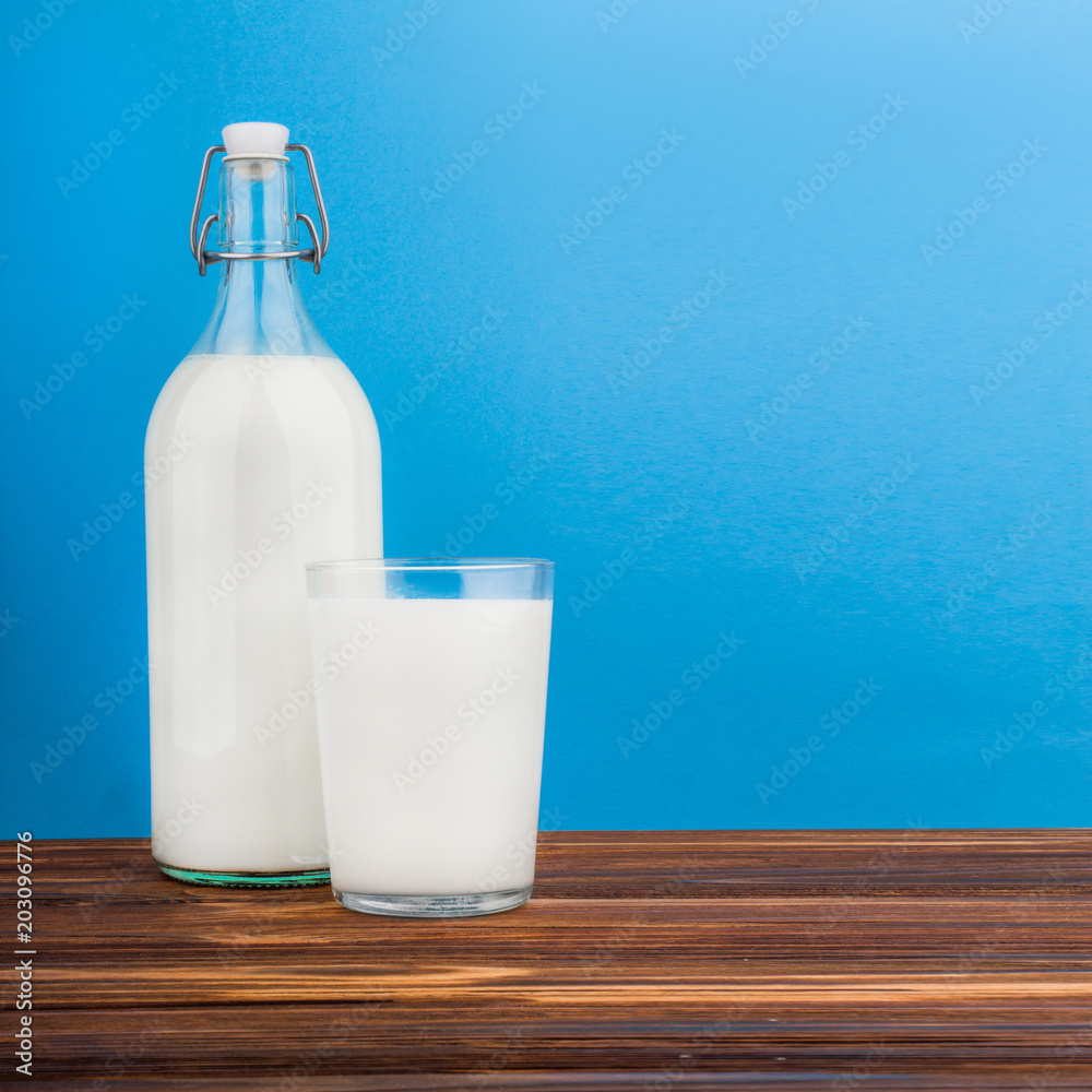 a glass of milk, a bottle of milk on a wooden table on a colored background a glass of milk, a bottle of milk on a wooden table on a colored background