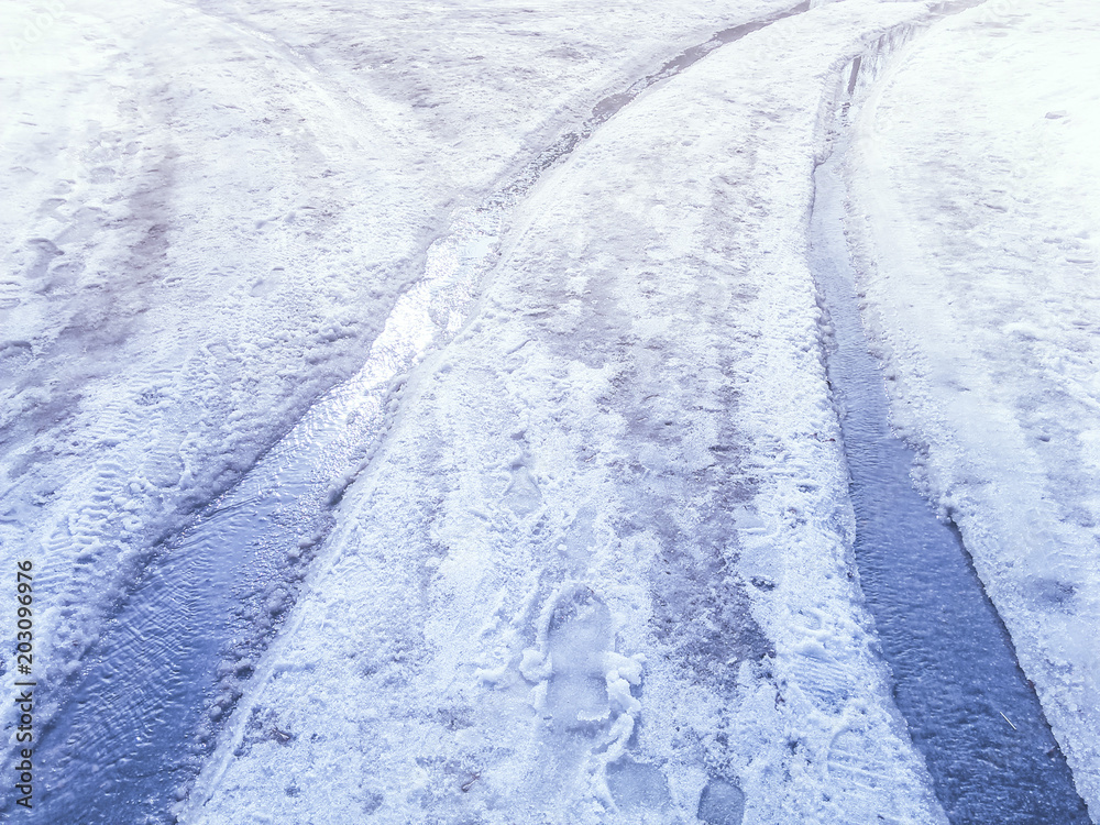 Obraz premium Streams of melted snow on a snowy road tracks in the spring day.