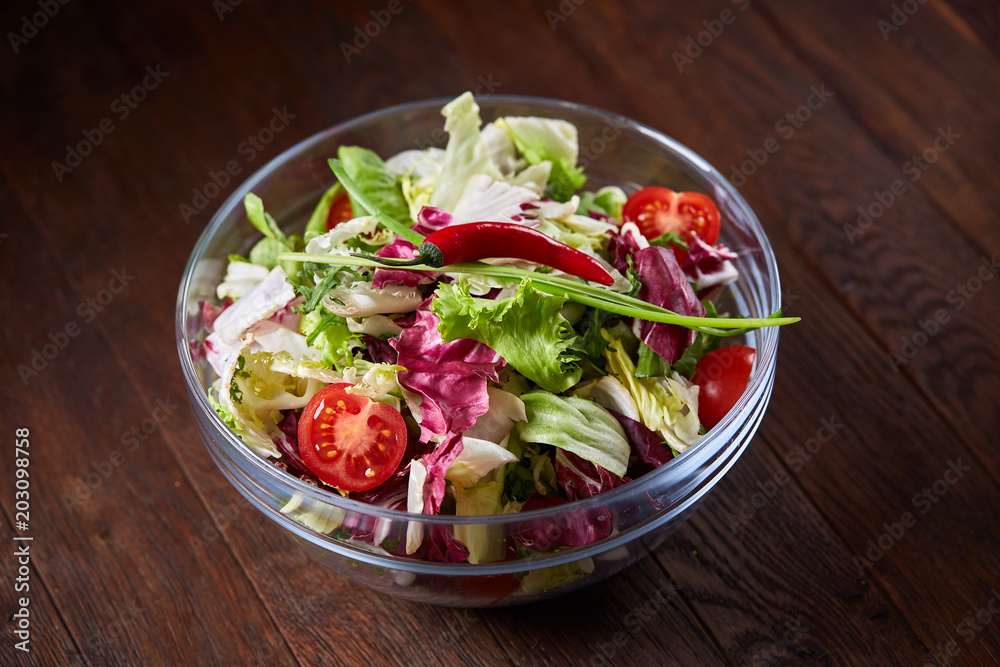 Fresh vegetable salad served in glass bowl over dark wooden background, selective focus, shallow depth of field Fresh vegetable salad served in glass bowl over dark wooden background, selective focus, shallow depth of field