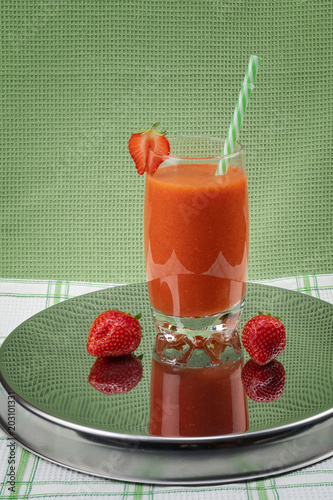Strawberry juice in a glass on a mirror tray on a green background