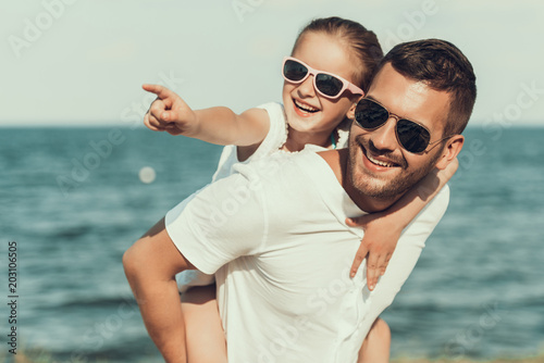Happy little daughter in sunglasses sits on fathers back. photo