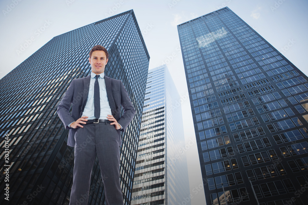 Happy businessman with hands on hips against low angle view of skyscrapers Happy businessman with hands on hips against low angle view of skyscrapers