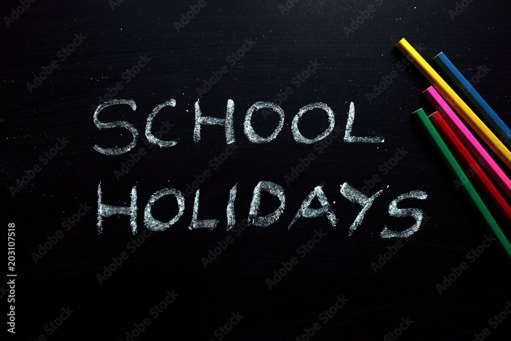 School holidays text and colored pencils on chalkboard School holidays text and colored pencils on chalkboard