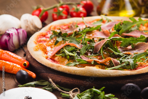 Pizza with bacon and arugula on a dark wooden background with ingredients around (close).