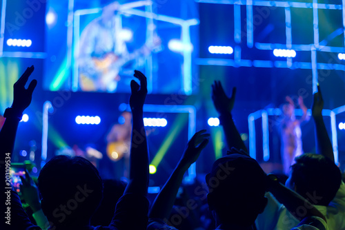 Crowd of hands up concert stage lights enjoying concert, and people fan audience silhouette raising hands in festival music rear view with spotlight glowing effect, blurred
