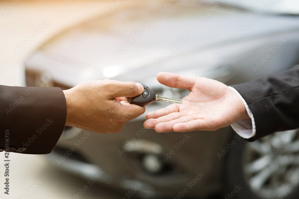 Car key, businessman handing over gives the car key to the other man on car background.