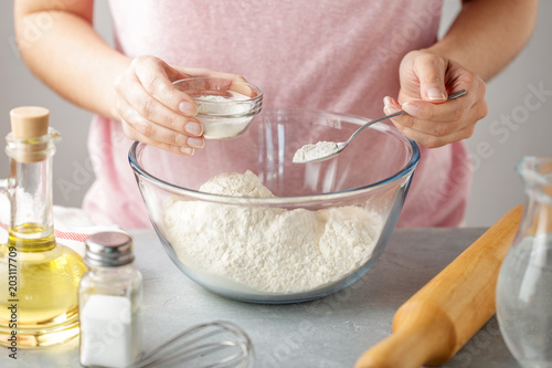 Women adds the baking powder into the glass bowl with flour. photo