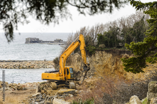 Excavator destroying a beach and a cliff for a hotel construction.