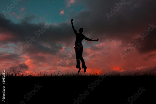 Silhouette of jumping woman against red sky over grass
