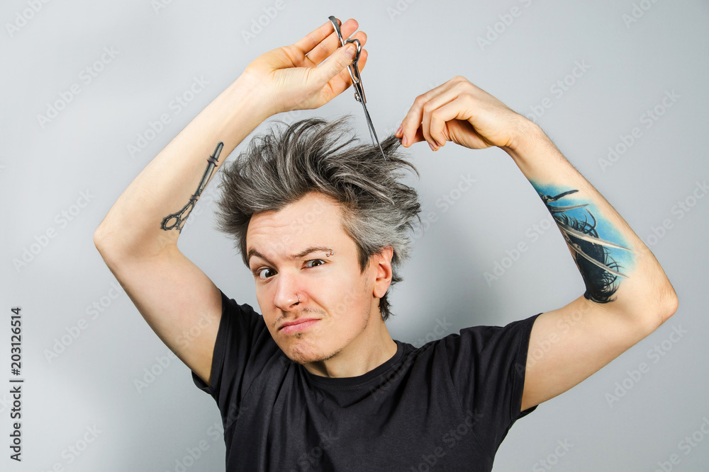 Unshorn and unshaven young guy with piercings on his face, shears her