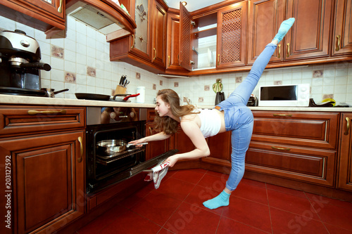 Sports woman in the kitchen, she cooks food and does exercises.