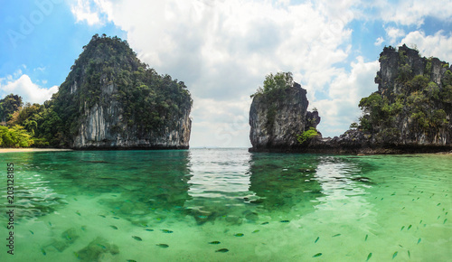Panorama of sharp karst cliffs rising from water with clear green sea full of fish in foreground. Hong Islands, Thailand