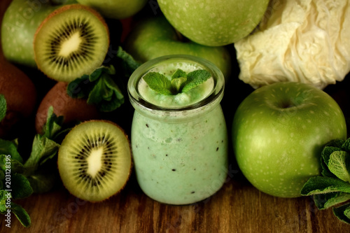 Green smoothie made of kiwi, apple and mint in glass jars surrounded by fruits
