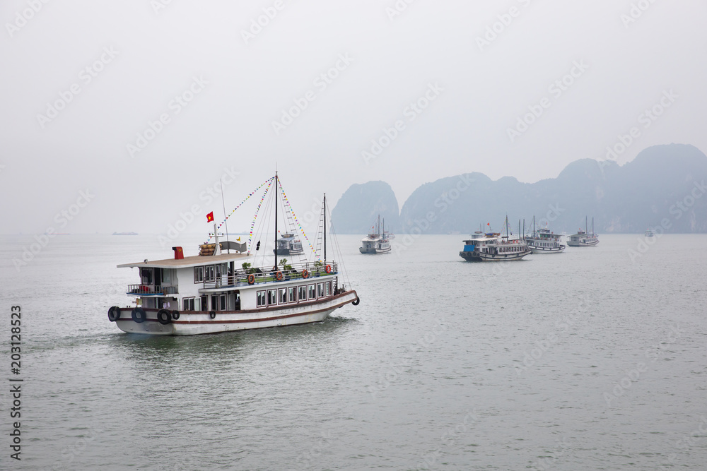 Big tourist cruise boat on the quiet water of Halong Bay (Unesco Heritage site) during late afternoon on the backdrop of a limestone rock mountain. Halong Bay, Vietnam. Big tourist cruise boat on the quiet water of Halong Bay (Unesco Heritage site) during late afternoon on the backdrop of a limestone rock mountain. Halong Bay, Vietnam.
